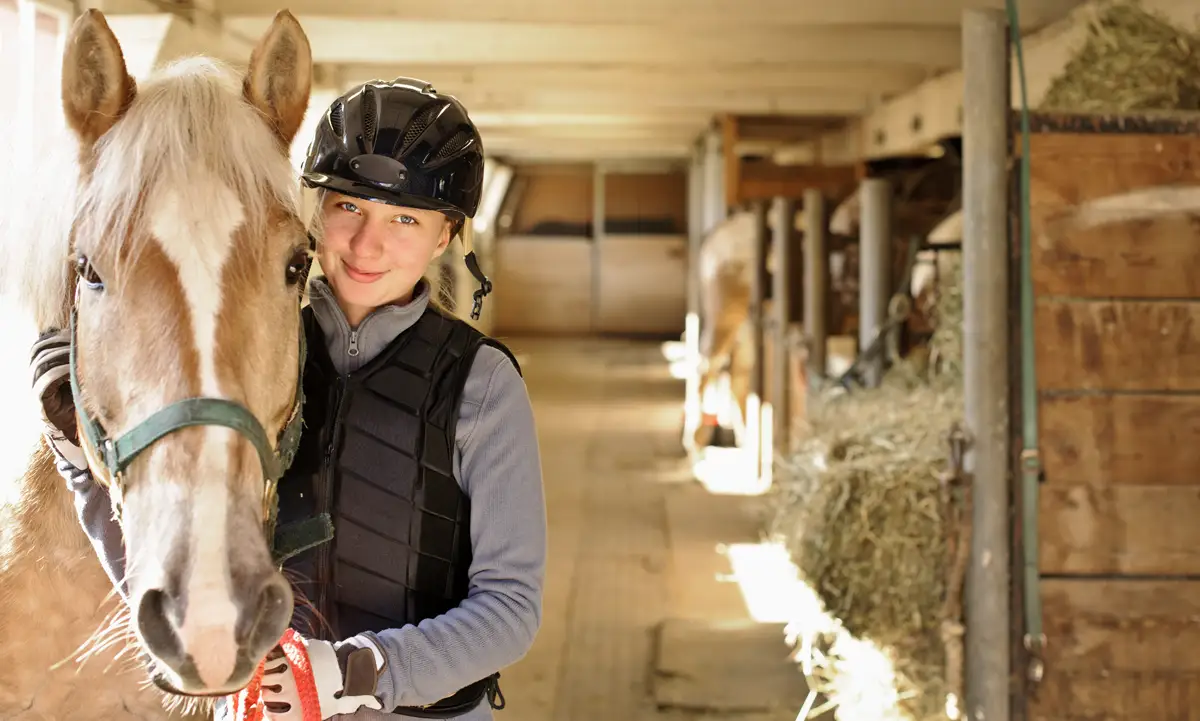 Young female rider with horse inside stable 